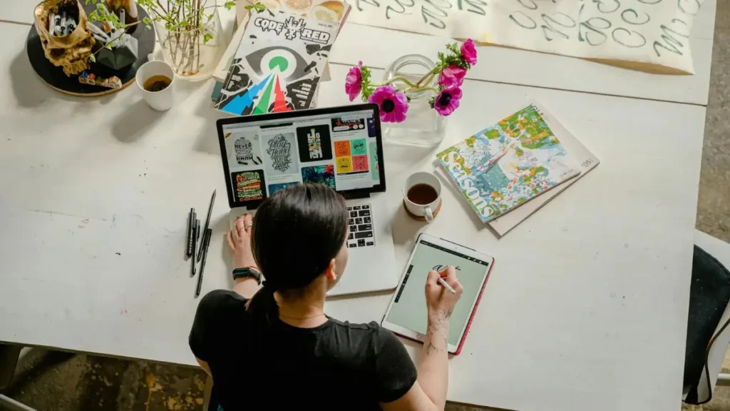 Graphic Design Blog Image: Woman at Laptop and Tablet Woman using a laptop and drawing on a tablet with a stylus, representing freelance graphic design work